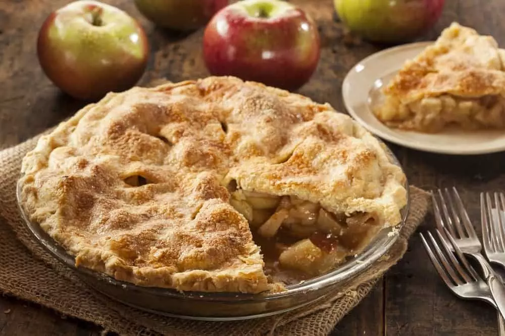 A delicious apple pie on a table with apples.