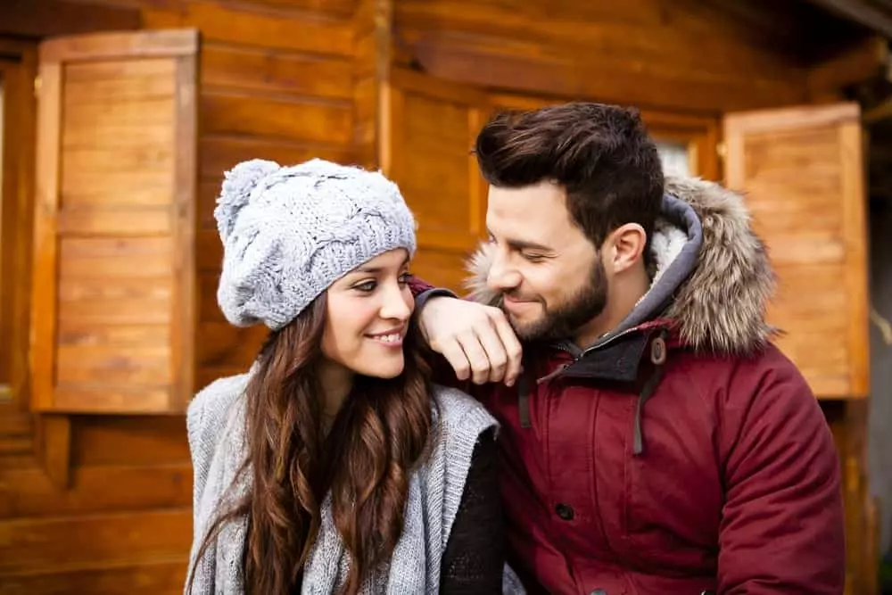 Young couple in winter clothes in front of their cabin