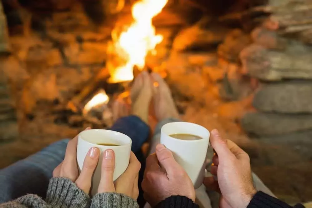 couple holding coffee in front of fire