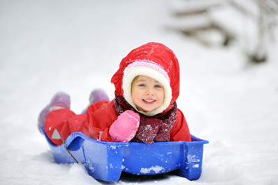 A little girl on a plastic sled on a snowy winter day.