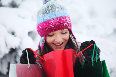 A woman looking inside a holiday gift bag with a snowy scene in the background.