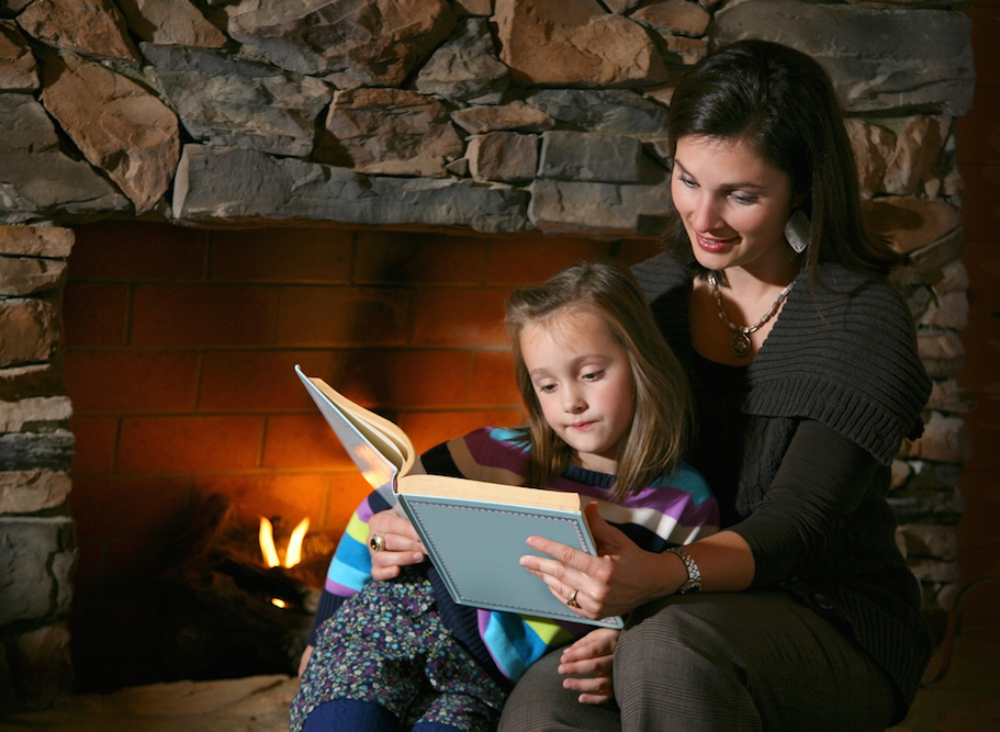 Mother and daughter reading a book together in front of the fireplace.