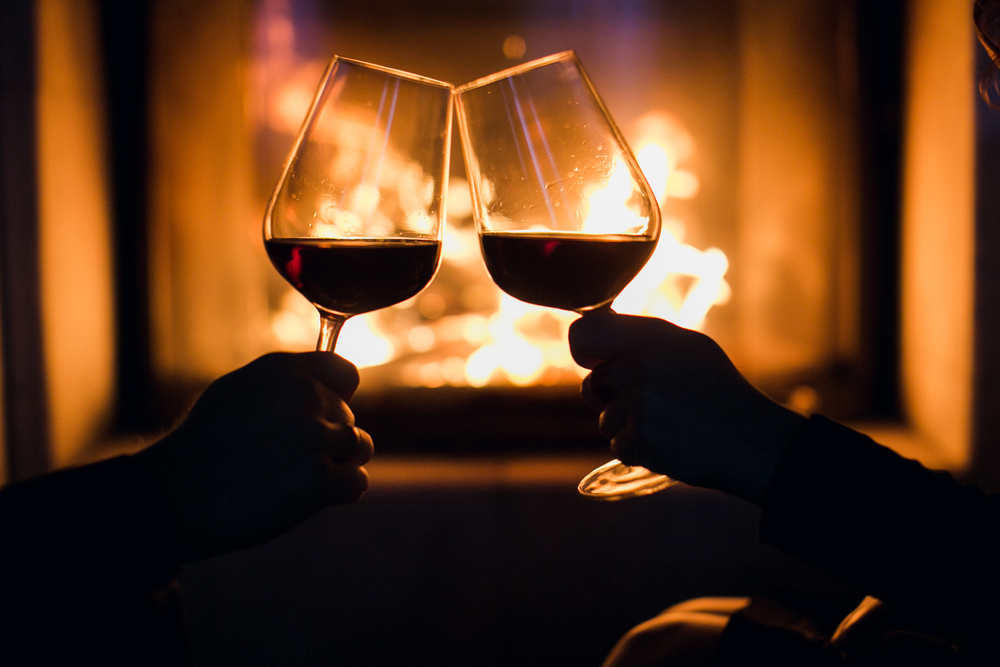 couple clinking glasses of wine in front of fireplace
