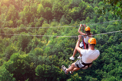 man and woman zip lining over green trees